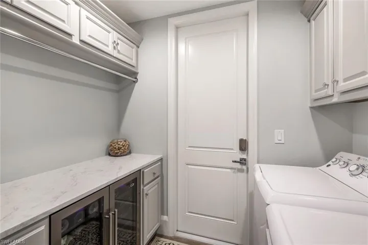 Laundry area featuring wine cooler, bar, washing machine and dryer, and cabinets