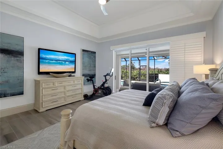 Bedroom featuring ornamental molding, access to exterior, wood-type flooring, and a raised ceiling