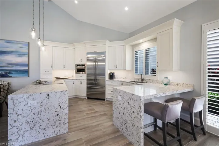Kitchen with kitchen peninsula, white cabinets, appliances with stainless steel finishes, light hardwood / wood-style floors, and decorative light fixtures