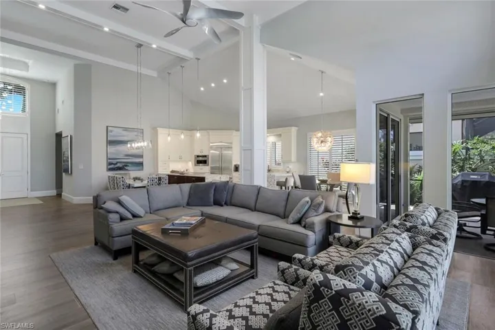 Living room with beamed ceiling, high vaulted ceiling, dark wood-type flooring, and ceiling fan with notable chandelier