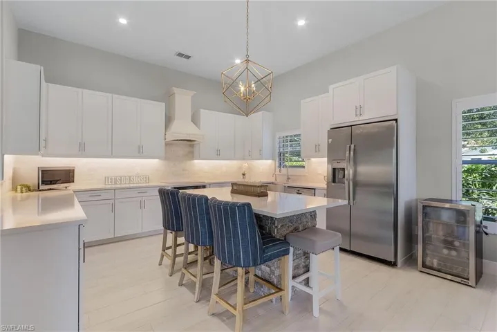 Kitchen with white cabinetry, appliances with stainless steel finishes, premium range hood, beverage cooler, and tasteful backsplash