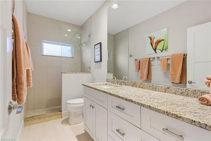 Bathroom with a tile shower, tile flooring, vanity with extensive cabinet space, and toilet