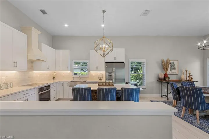Kitchen with hanging light fixtures, light wood-type flooring, custom range hood, appliances with stainless steel finishes, and backsplash