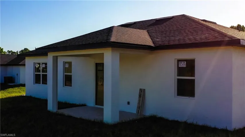 Rear view of house featuring stucco siding, a lawn, and roof with shingles