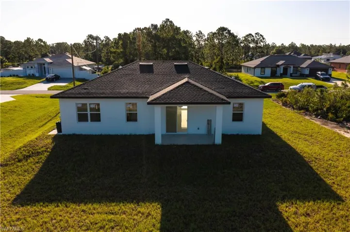 Rear view of property with stucco siding, a yard, a residential view, and view of wooded area