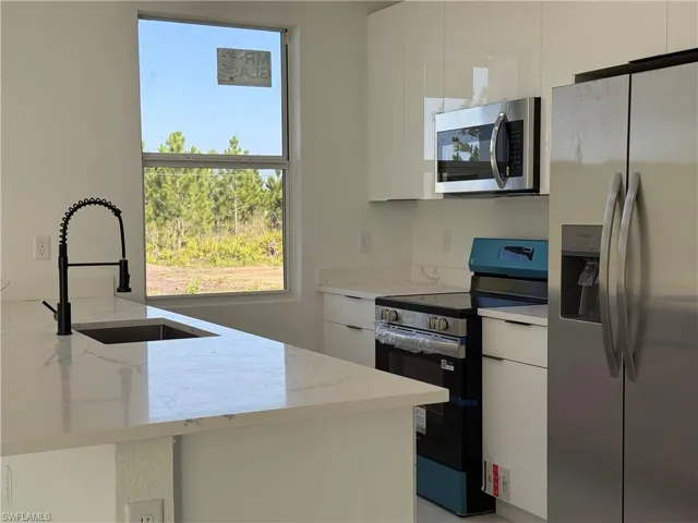 Kitchen featuring stainless steel appliances, modern cabinets, white cabinetry, and light stone counters