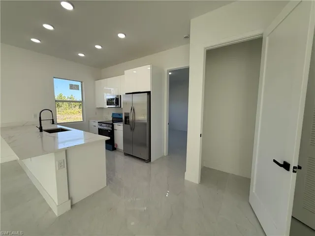 Kitchen with stainless steel appliances, white cabinets, a peninsula, modern cabinets, and light stone countertops