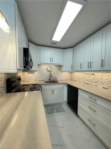 Kitchen with dishwashing machine, stove, white cabinetry, and sink