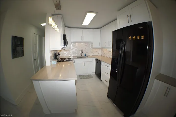 Kitchen with marble finish floor, a peninsula, a sink, backsplash, and black appliances