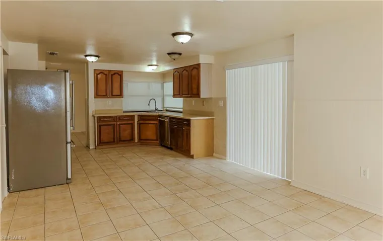 Kitchen featuring appliances with stainless steel finishes, brown cabinetry, light countertops, a wainscoted wall, and light tile patterned floors