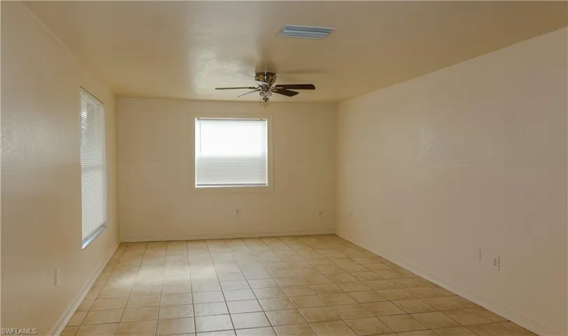 Empty room with a ceiling fan and light tile patterned flooring