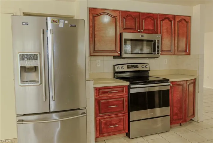 Kitchen featuring appliances with stainless steel finishes, reddish brown cabinets, light countertops, and light tile patterned flooring