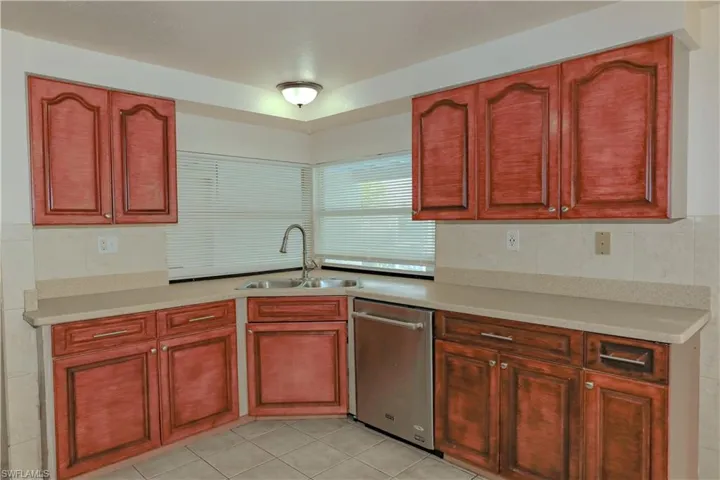 Kitchen featuring stainless steel dishwasher, dark brown cabinets, and light tile patterned floors