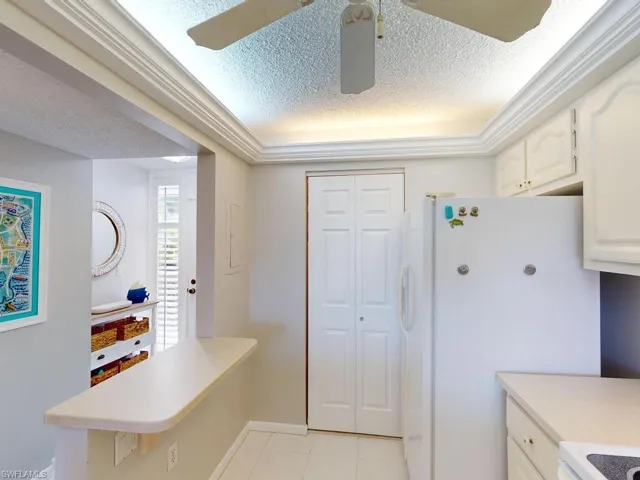 Kitchen with white cabinets, light tile patterned floors, white refrigerator, ceiling fan, and a textured ceiling