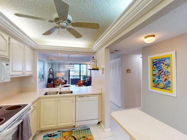 Kitchen featuring light tile patterned floors, white appliances, sink, ceiling fan, and a textured ceiling