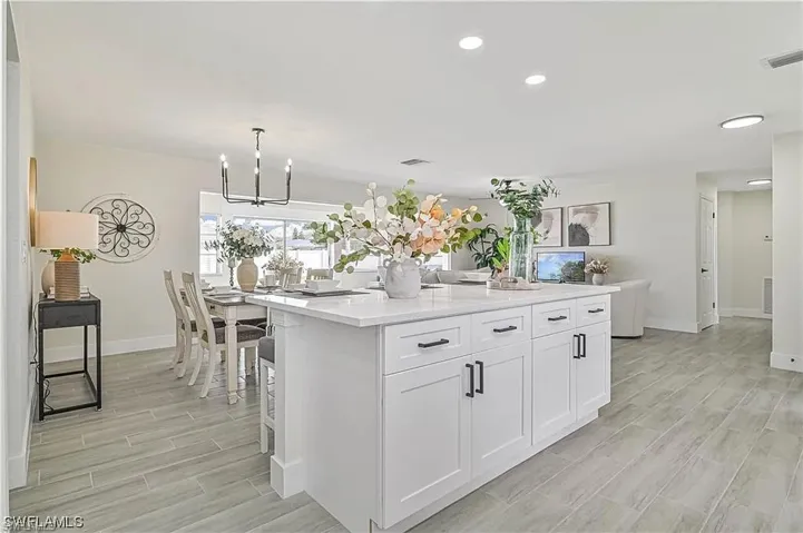 The property features an open living space with light-colored flooring, a modern kitchen island with white cabinetry, and recessed lighting throughout