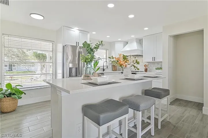 Well-appointed kitchen featuring white cabinetry, a large kitchen island with seating, a stainless steel refrigerator, and recessed lighting