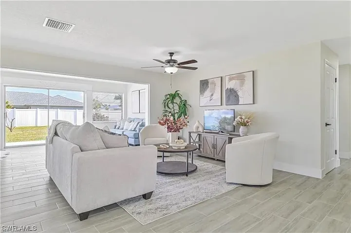 This spacious living area features light-toned tiled flooring, large windows, and a ceiling fan