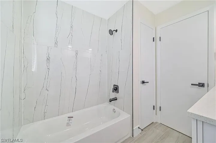 Bathroom featuring a white bathtub, white marble-patterned shower tiling, and dark-toned fixtures