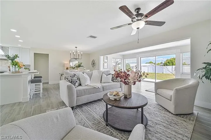 Spacious open-concept living area featuring light-toned flooring, a ceiling fan, and large sliding glass doors that open to a verdant outdoor space