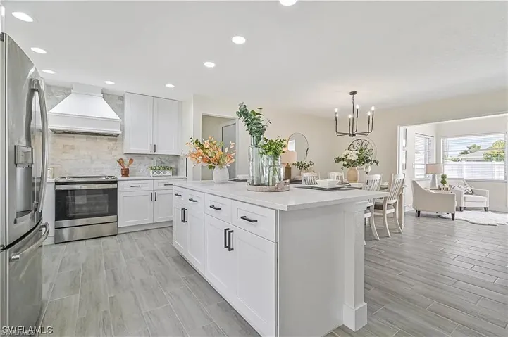 The kitchen features white cabinetry, stainless steel appliances, and a central island with a light-colored countertop, complemented by recessed lighting and light-toned flooring