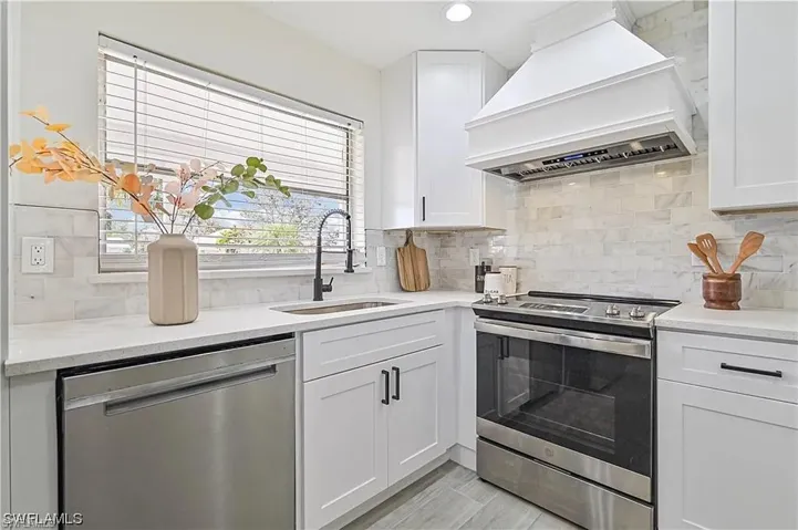 The kitchen features white cabinetry, a stainless steel dishwasher, a stainless steel range with an overhead hood, and a white tile backsplash