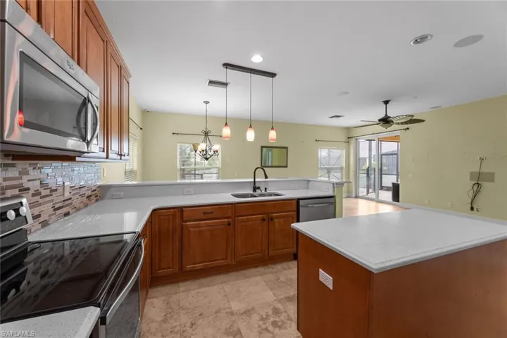 Kitchen featuring kitchen peninsula, stainless steel appliances, ceiling fan with notable chandelier, hanging light fixtures, and sink