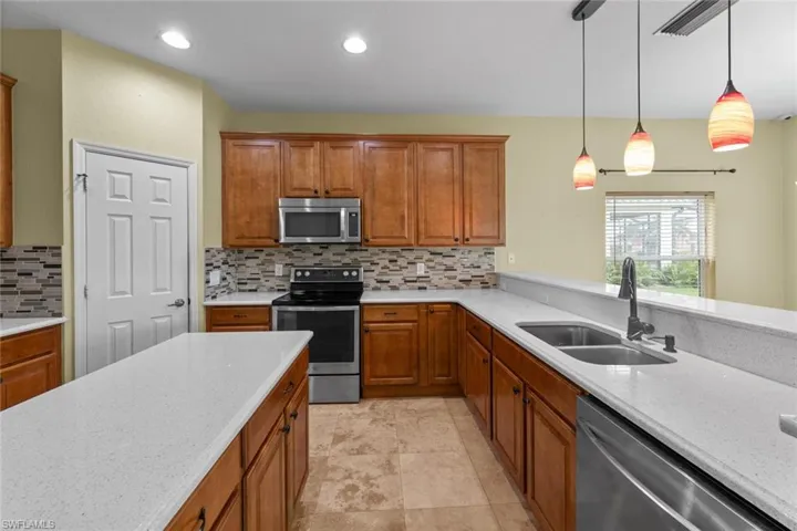 Kitchen featuring stainless steel appliances, pendant lighting, backsplash, light tile floors, and sink