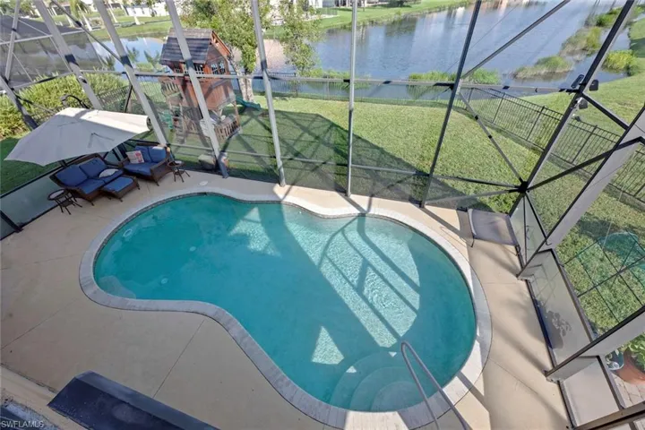 View of swimming pool featuring glass enclosure, a water view, a patio area, and a lawn