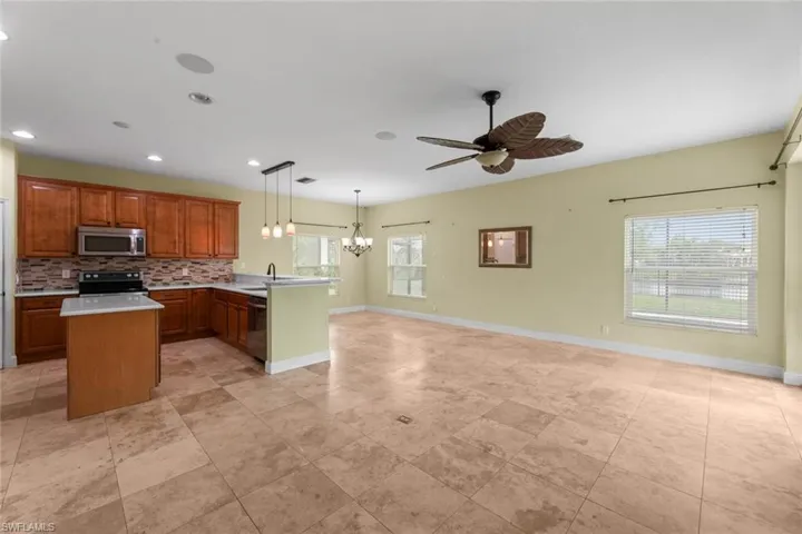 Kitchen with stainless steel appliances, decorative light fixtures, ceiling fan with notable chandelier, backsplash, and light tile floors