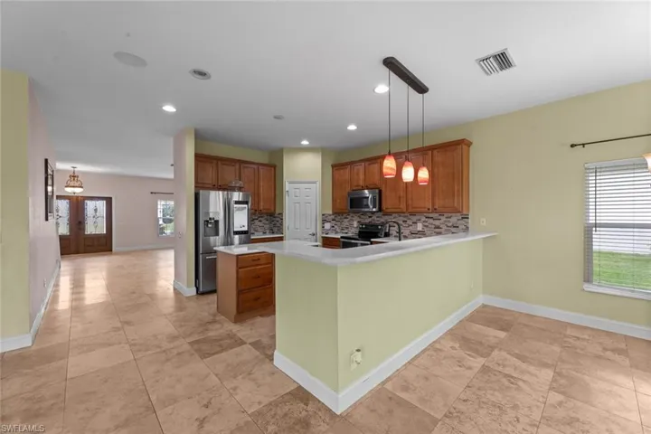 Kitchen featuring hanging light fixtures, stainless steel appliances, backsplash, and light tile floors