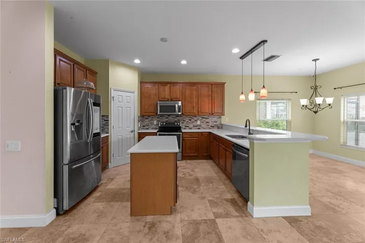 Kitchen featuring a kitchen island, backsplash, appliances with stainless steel finishes, light tile floors, and pendant lighting