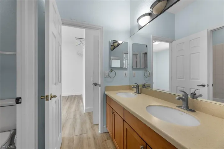 Bathroom with vanity with extensive cabinet space, dual sinks, toilet, and hardwood / wood-style flooring