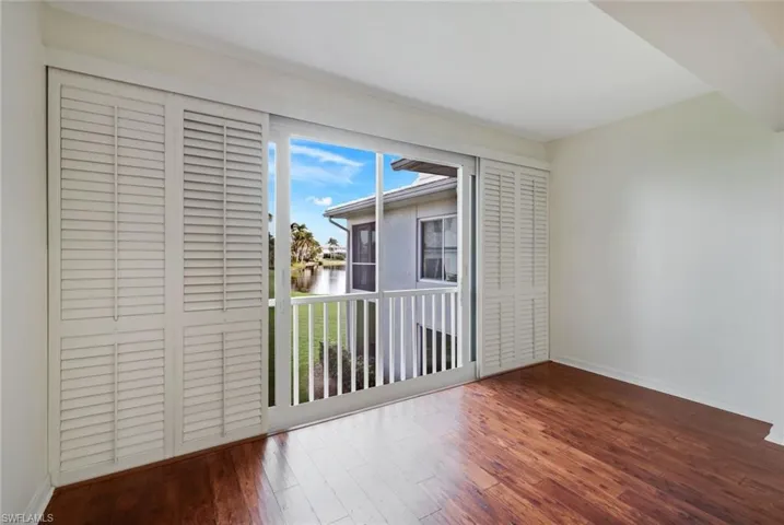 Unfurnished bedroom with dark wood finished floors, a water view, and access to exterior