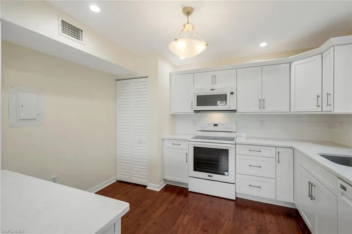 Kitchen featuring white appliances, white cabinets, decorative light fixtures, light stone counters, and tasteful backsplash