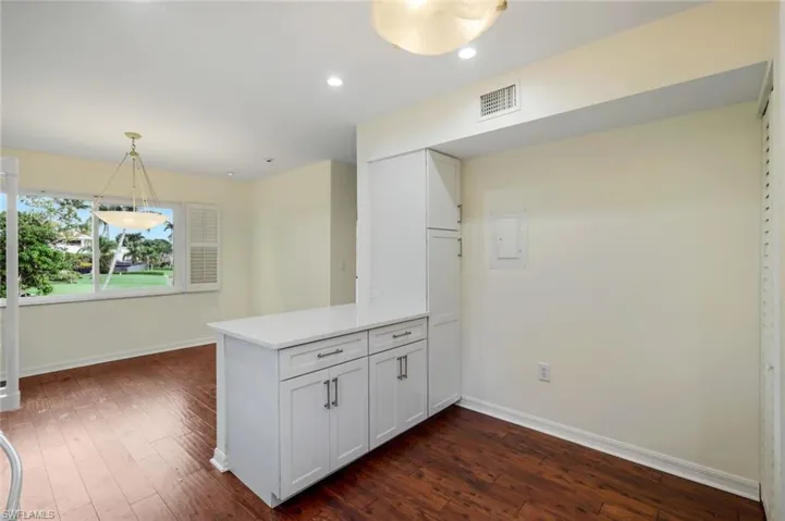 Kitchen featuring white cabinetry, a peninsula, decorative light fixtures, dark wood-type flooring, and recessed lighting