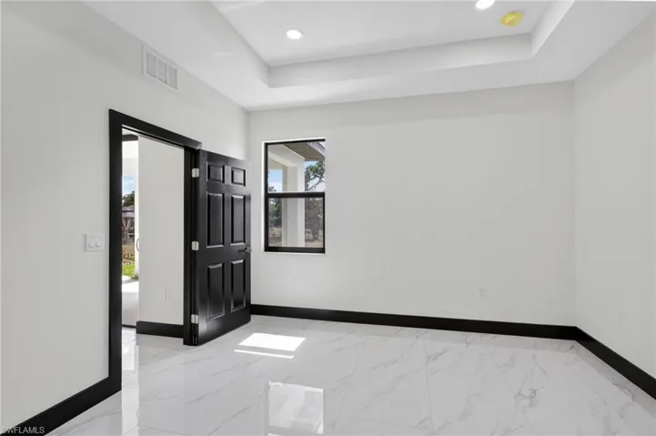 Spare room with a raised ceiling, light marble finish flooring, and recessed lighting