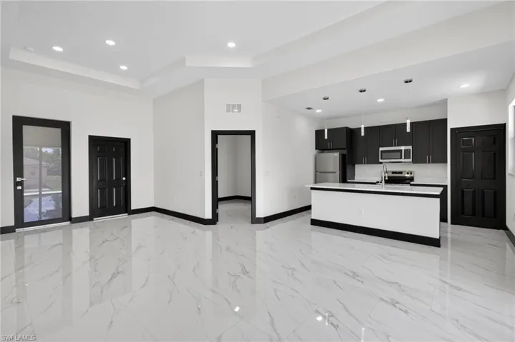 Kitchen featuring dark cabinetry, open floor plan, light marble finish floors, a kitchen island with sink, and stainless steel appliances