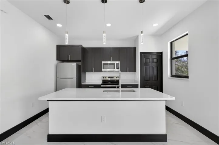 Kitchen with stainless steel appliances, a center island with sink, hanging light fixtures, and dark cabinetry