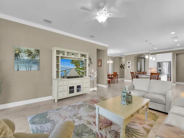 Tiled living room with ornamental molding and ceiling fan with notable chandelier