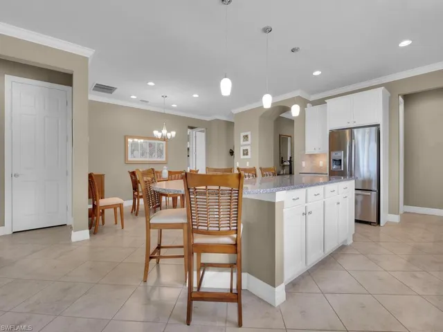 Kitchen featuring stainless steel fridge, light stone counters, a kitchen island, white cabinetry, and decorative light fixtures