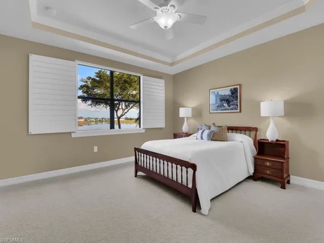 Bedroom with ceiling fan, light colored carpet, a water view, and a raised ceiling