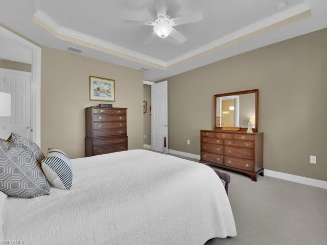 Carpeted bedroom featuring ornamental molding, a tray ceiling, and ceiling fan