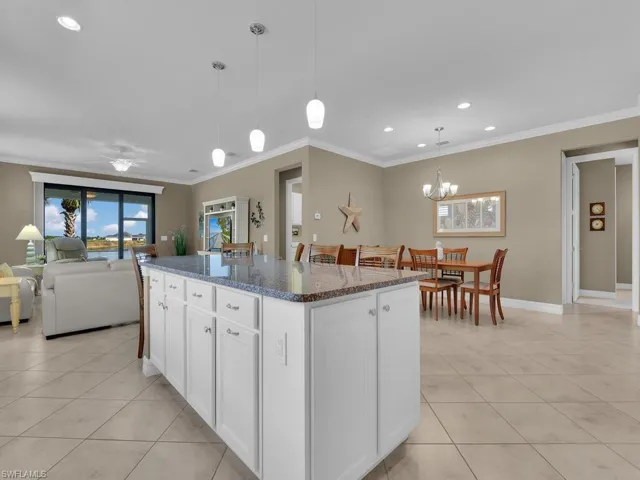 Kitchen with a kitchen island, white cabinetry, dark stone counters, decorative light fixtures, and crown molding