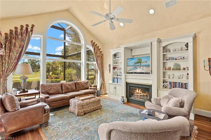 Living area featuring visible vents, high vaulted ceiling, a ceiling fan, a glass covered fireplace, and wood finished floors
