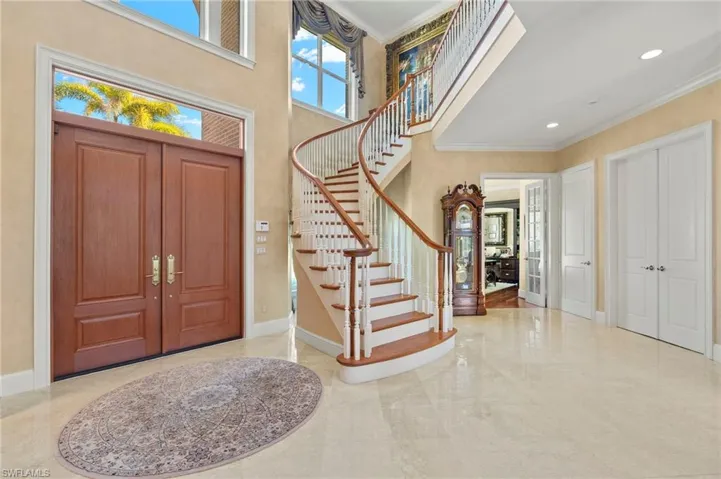 Foyer entrance with marble finish floor, ornamental molding, stairway, baseboards, and a towering ceiling