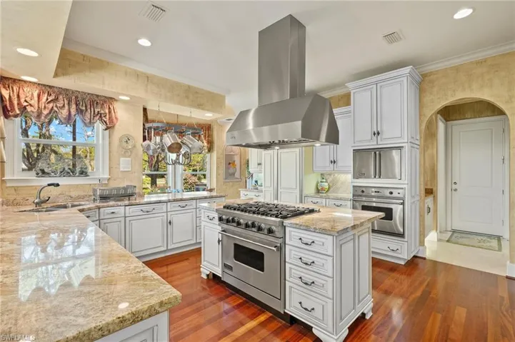 Kitchen featuring visible vents, light stone countertops, ornamental molding, island range hood, and stainless steel appliances