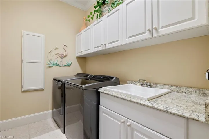 Laundry room with washing machine and clothes dryer, baseboards, tile patterned floors, cabinet space, and a sink