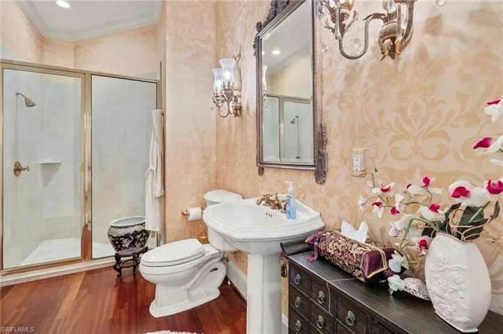 Full bathroom with wood finished floors, wallpapered walls, a stall shower, a sink, and toilet