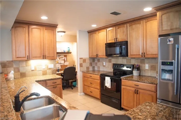 Kitchen with light tile patterned flooring, black appliances, decorative backsplash, sink, and light stone counters